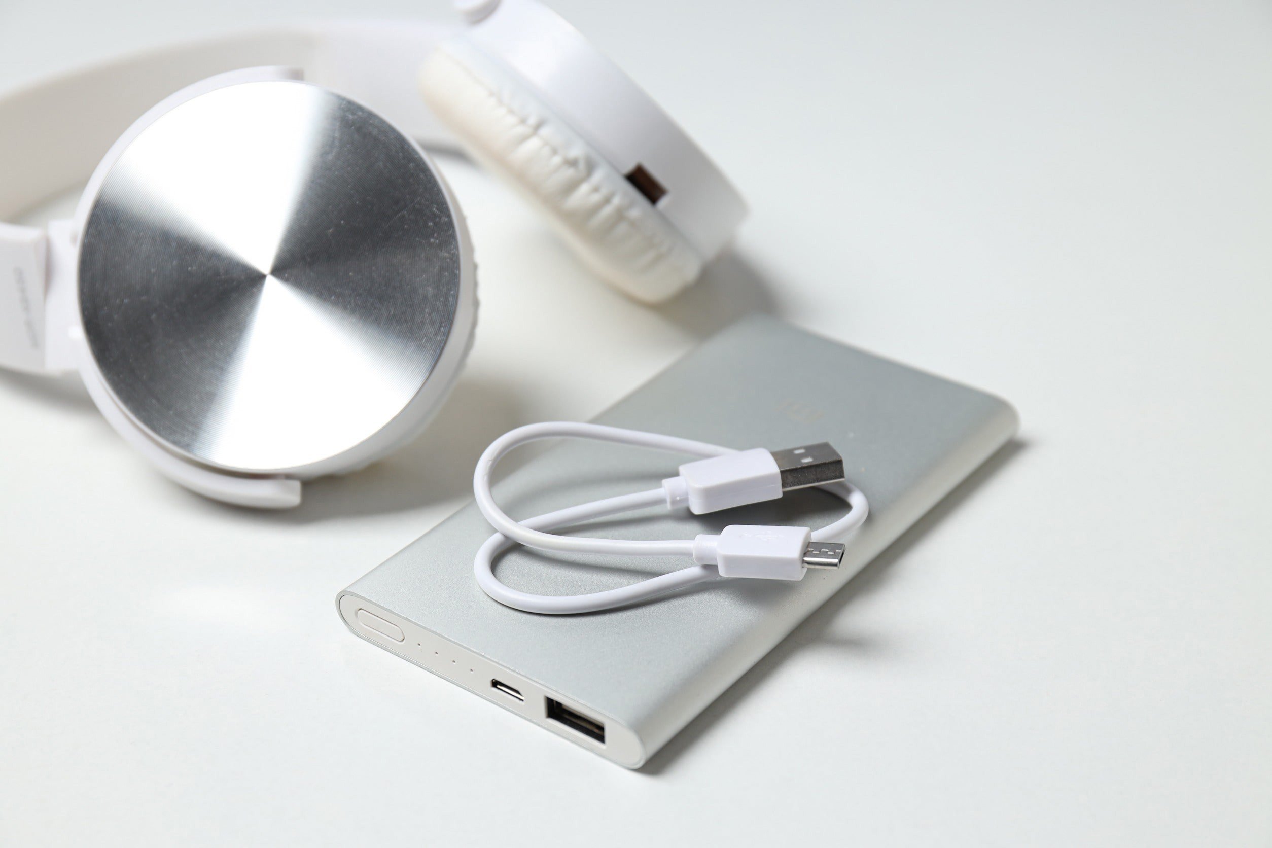 White and silver headphones lying next to a gray power bank against a white background