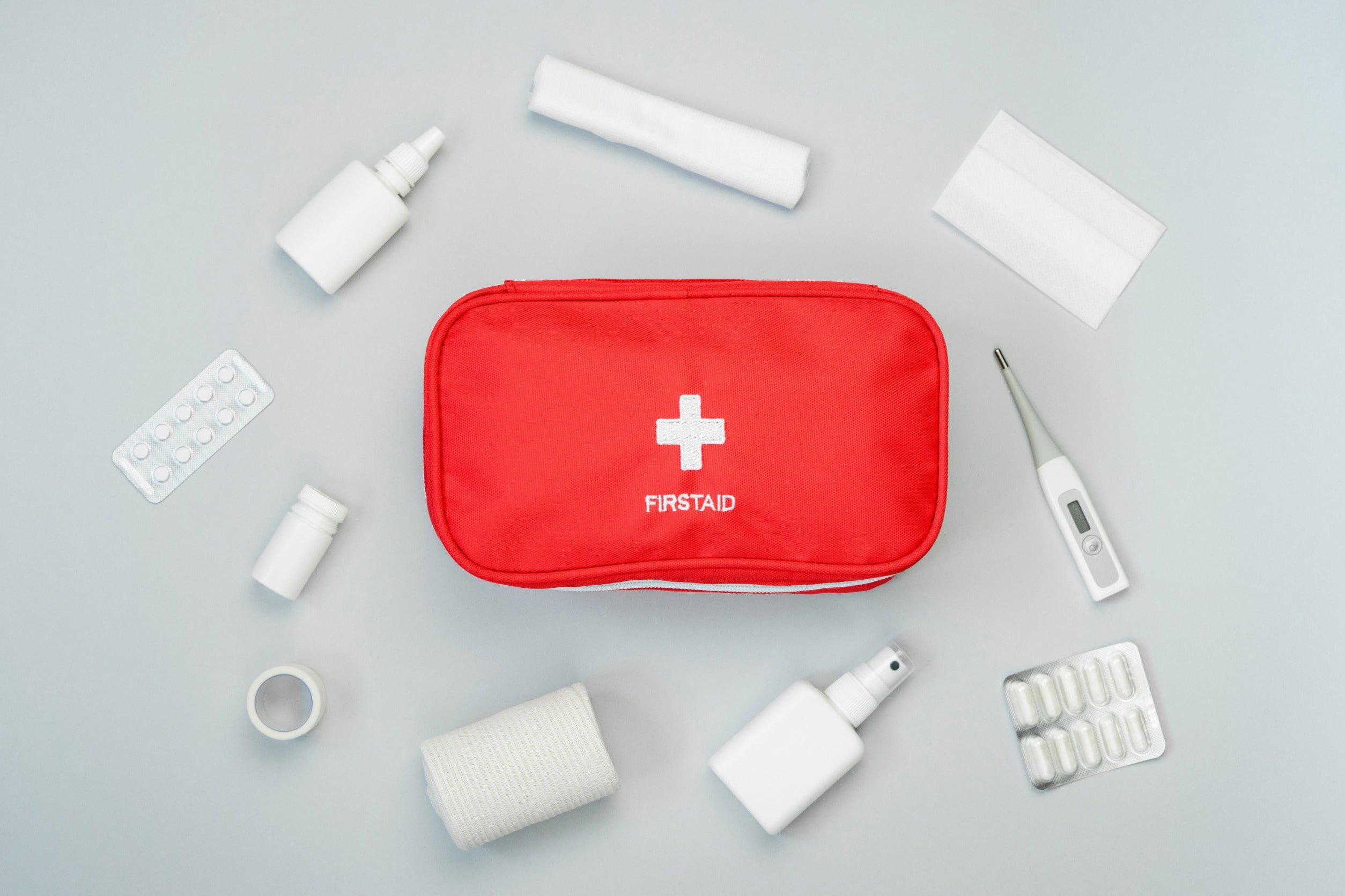 Red first aid bag with bandages and various other hospital items around it against a grey background