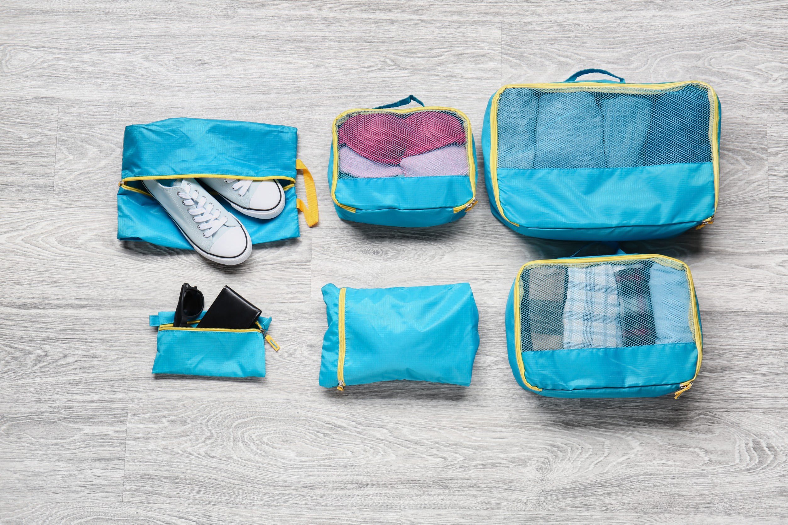 Six different packing bags in blue on a grey floor to be put in a suitcase