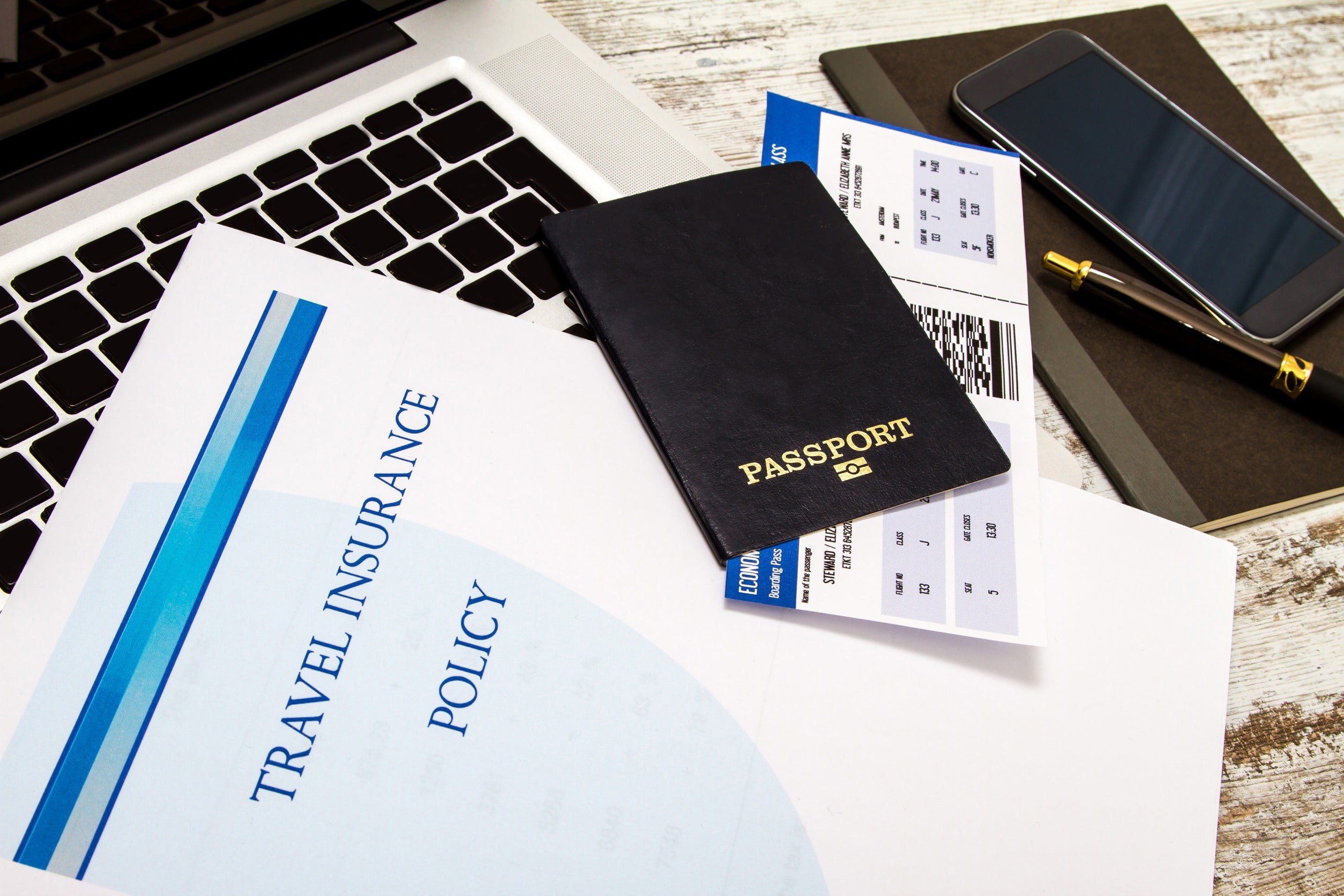 Papers with travel insurance and passport are on a laptop ready for a trip abroad