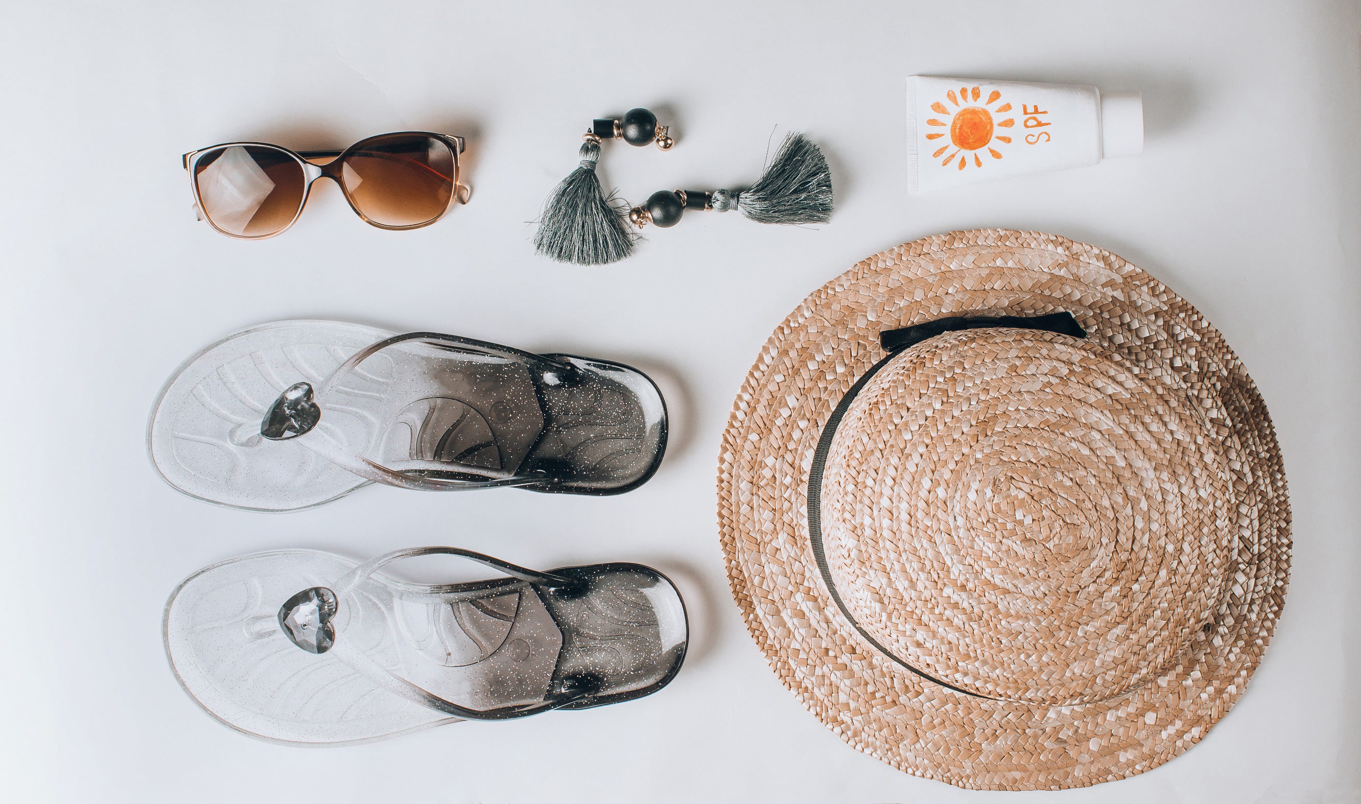 Sunglasses, flip-flops, hat and sunscreen on a white table