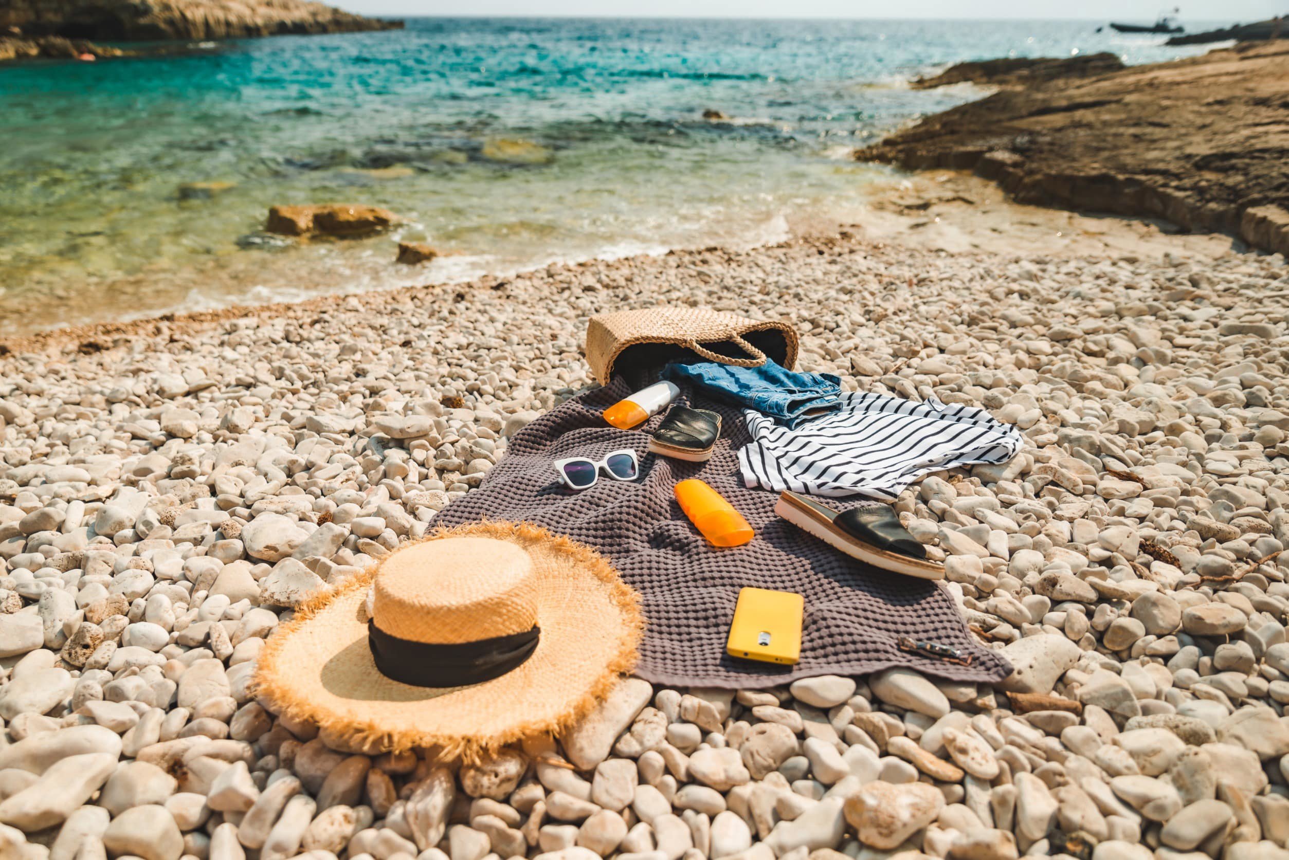 A hat, bag and towel on a rocky beach with beautiful blue sea in the background