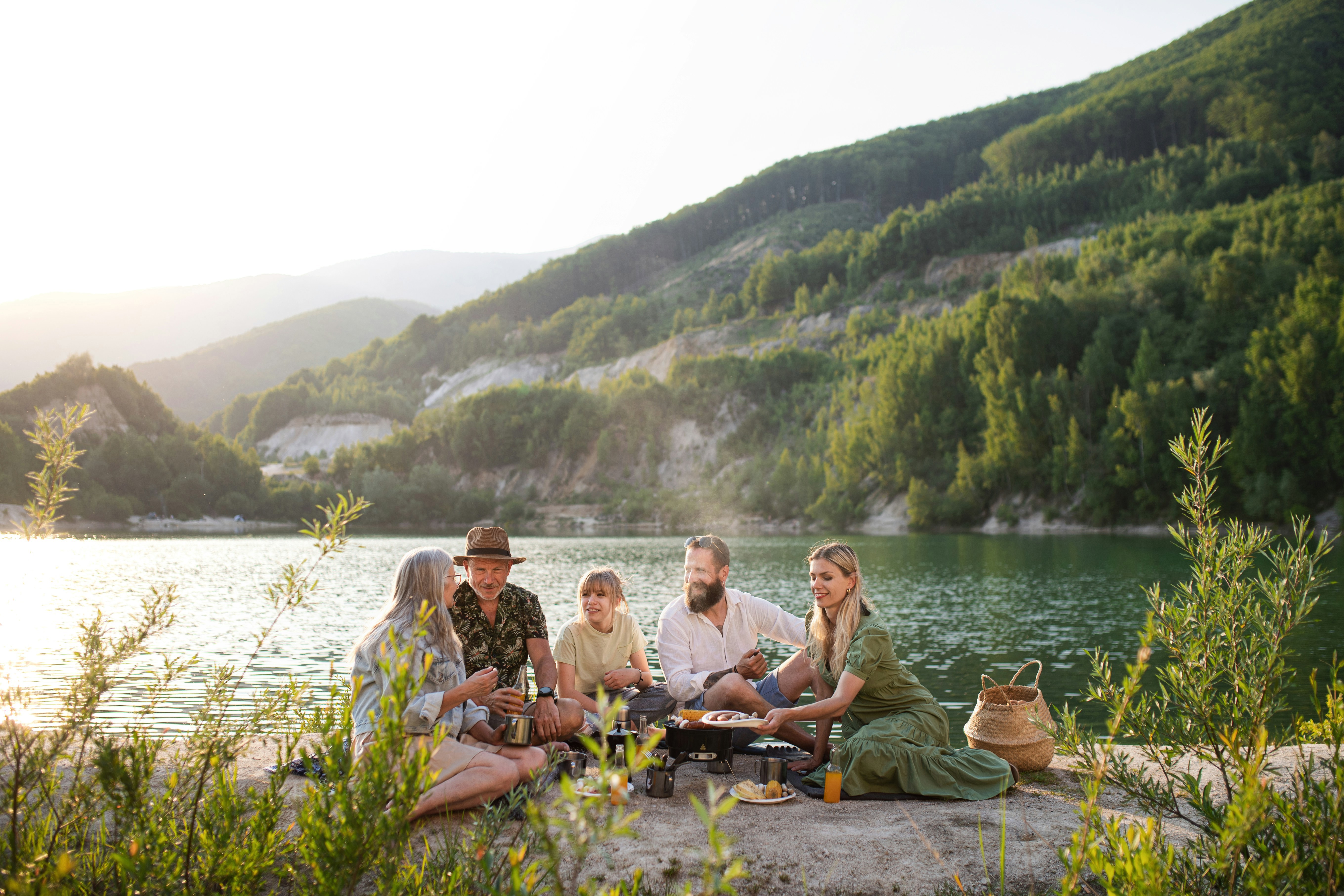 A group of friends are sitting by a lake and hanging out with beautiful mountains in the background