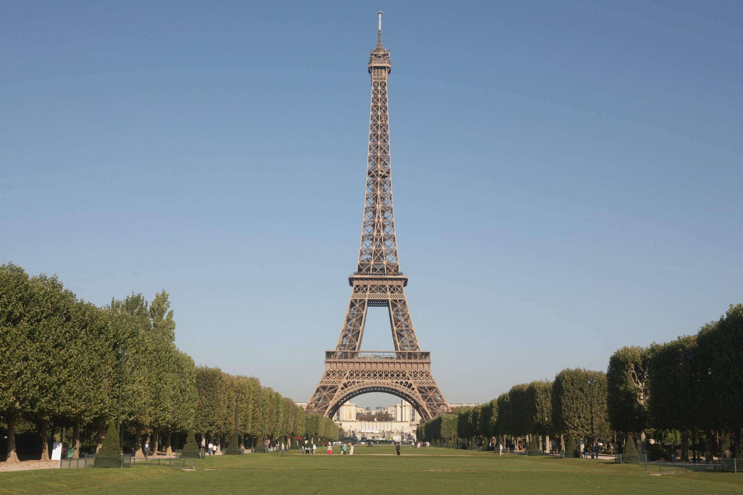 View of the Eiffel Tower below a large green lawn led with beautiful trees on the sides