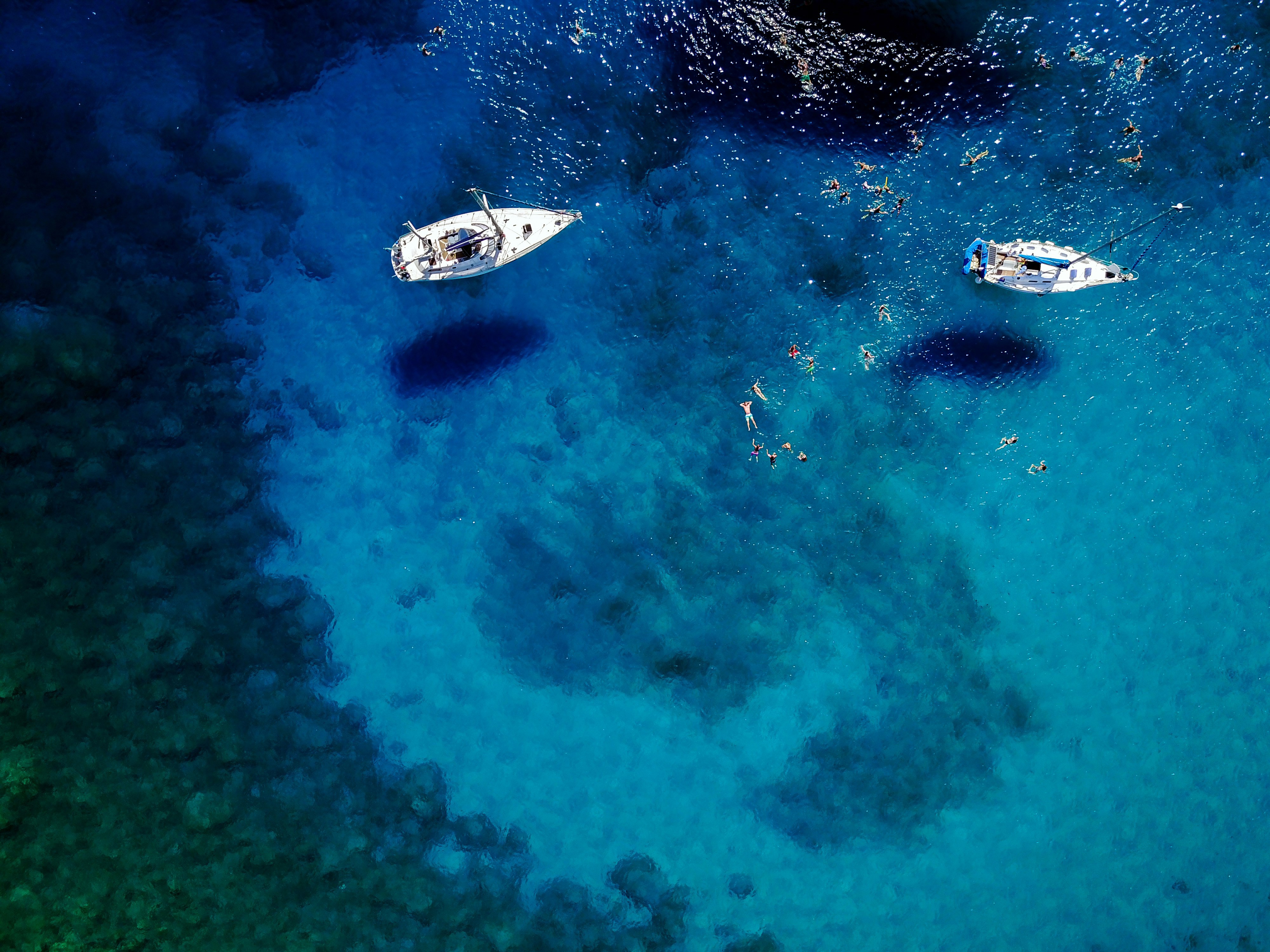 Book travel experience - Aerial view of two pleasure boats on crystal clear blue water with swimmers.