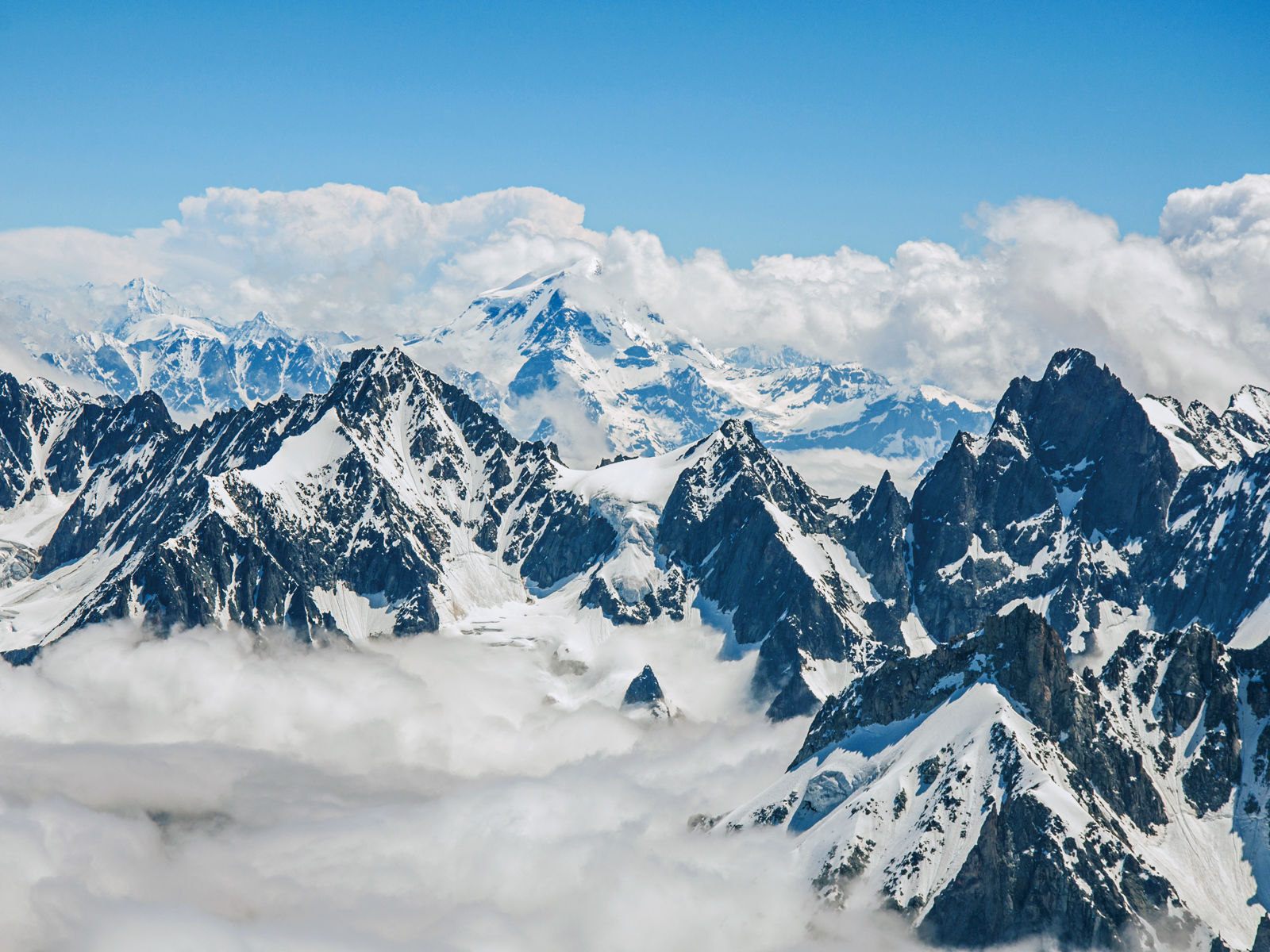 Høje snedækkede bjerge i Alperne med blå himmel i baggrunden
