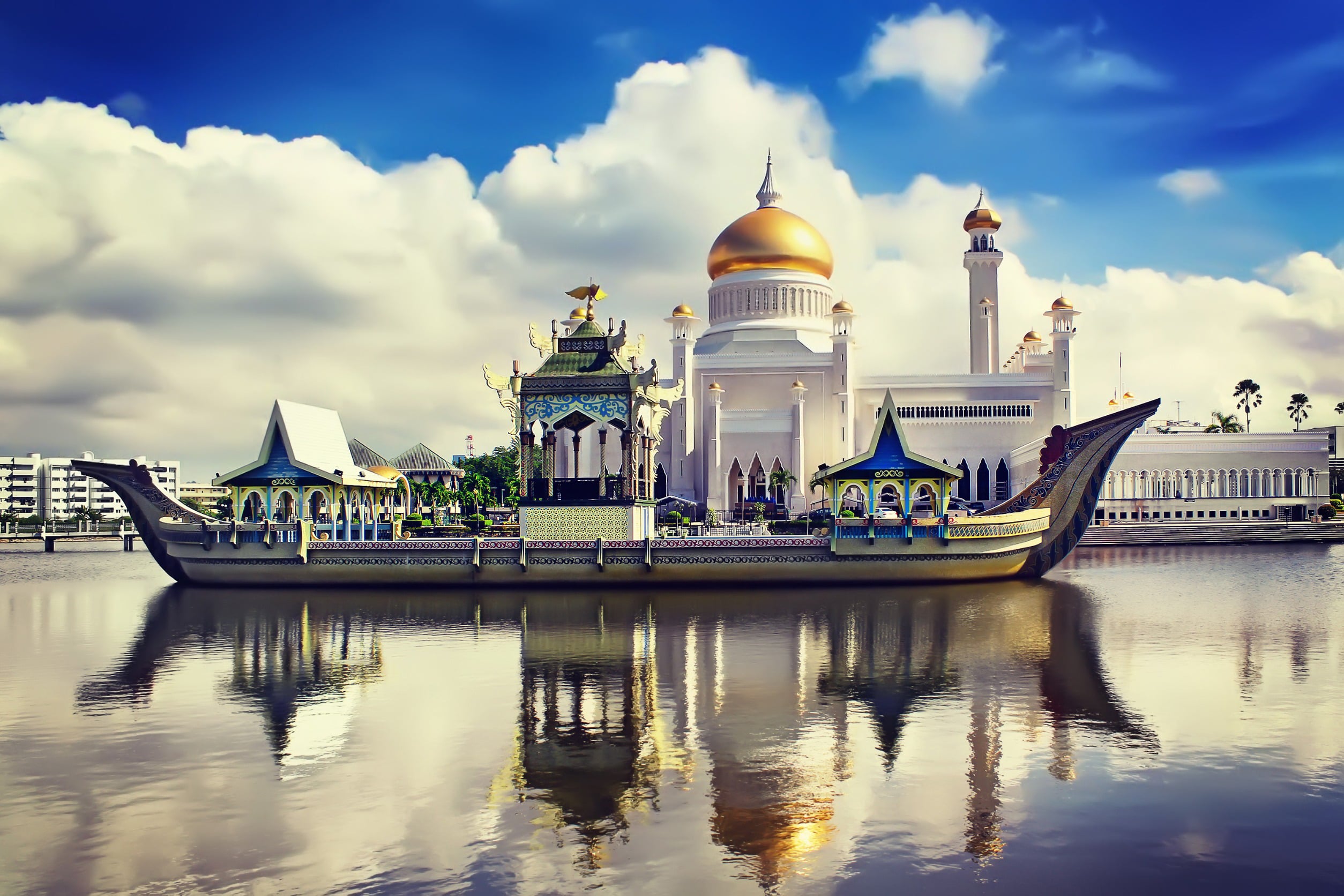 View from a river up to a beautiful boat in front of a white temple with golden peaks and blue sky in the background