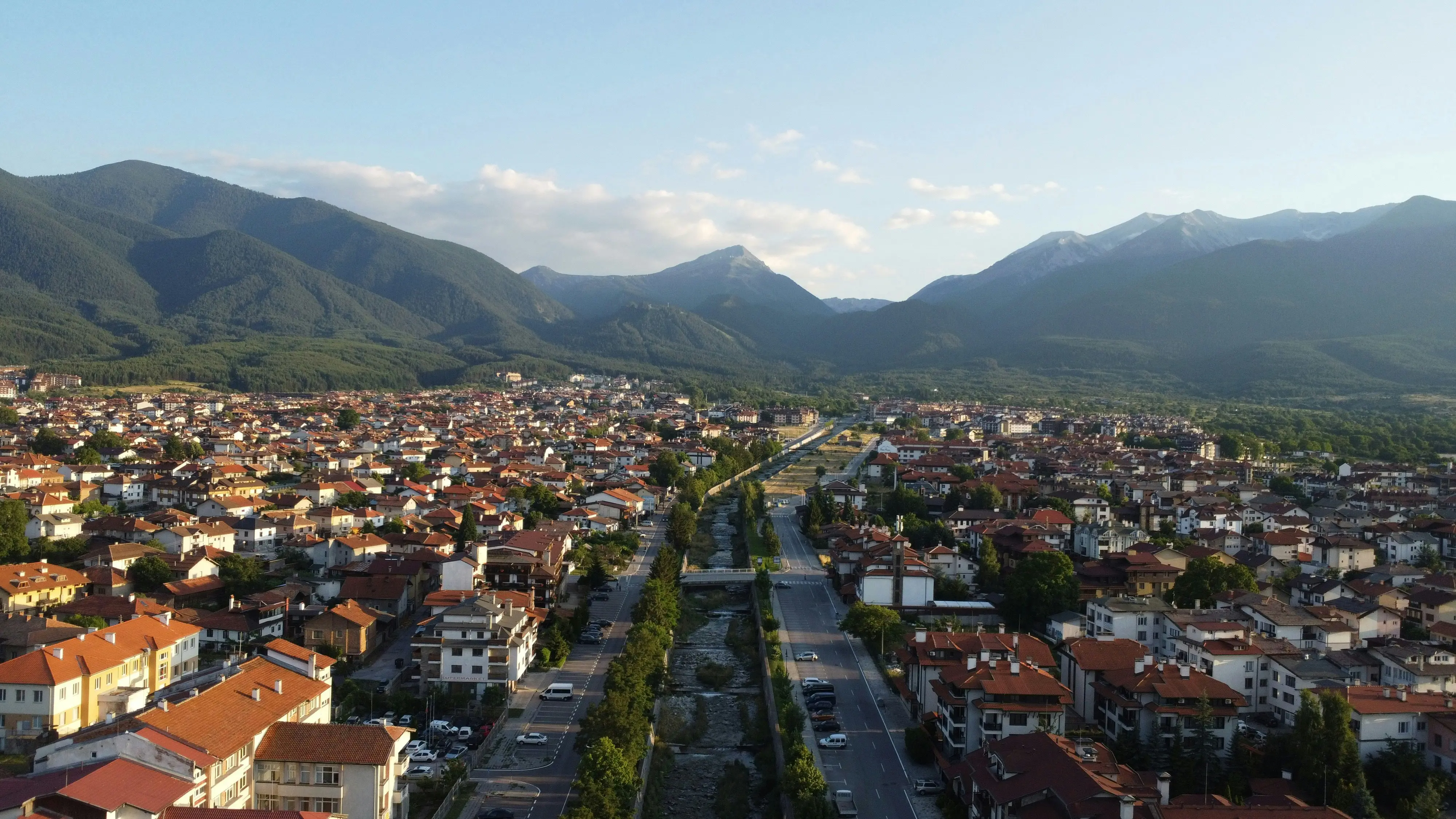 Travel to Bansko - Small town view surrounded by green mountains and forests under bright morning sky