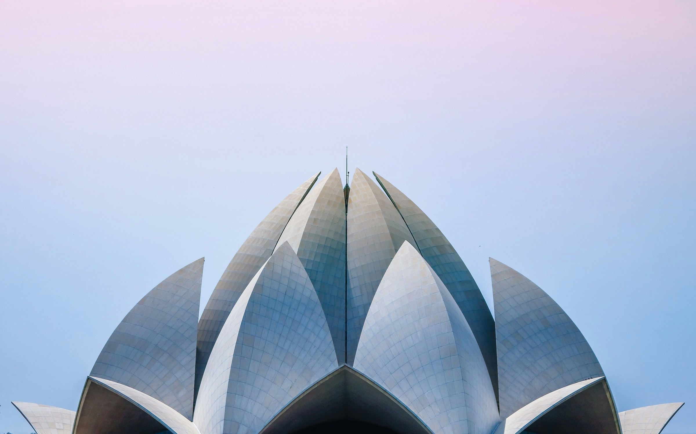 Symmetrisk udsigt over en moderne bygning med lotuslignende struktur mod en pastelfarvet himmel i Delhi.
