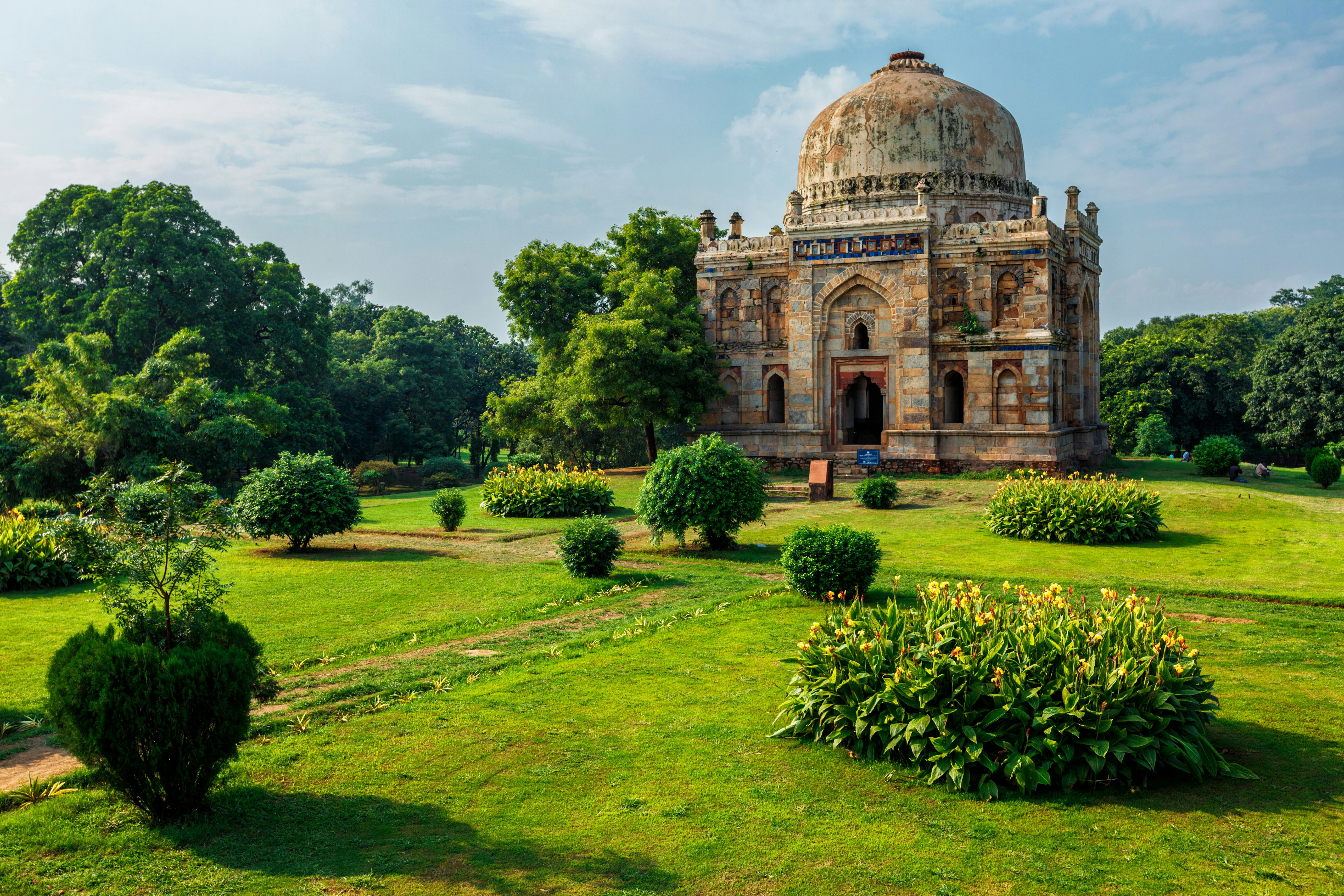 Frodig have og historisk kuppelformet bygning under klar blå himmel i Delhi.