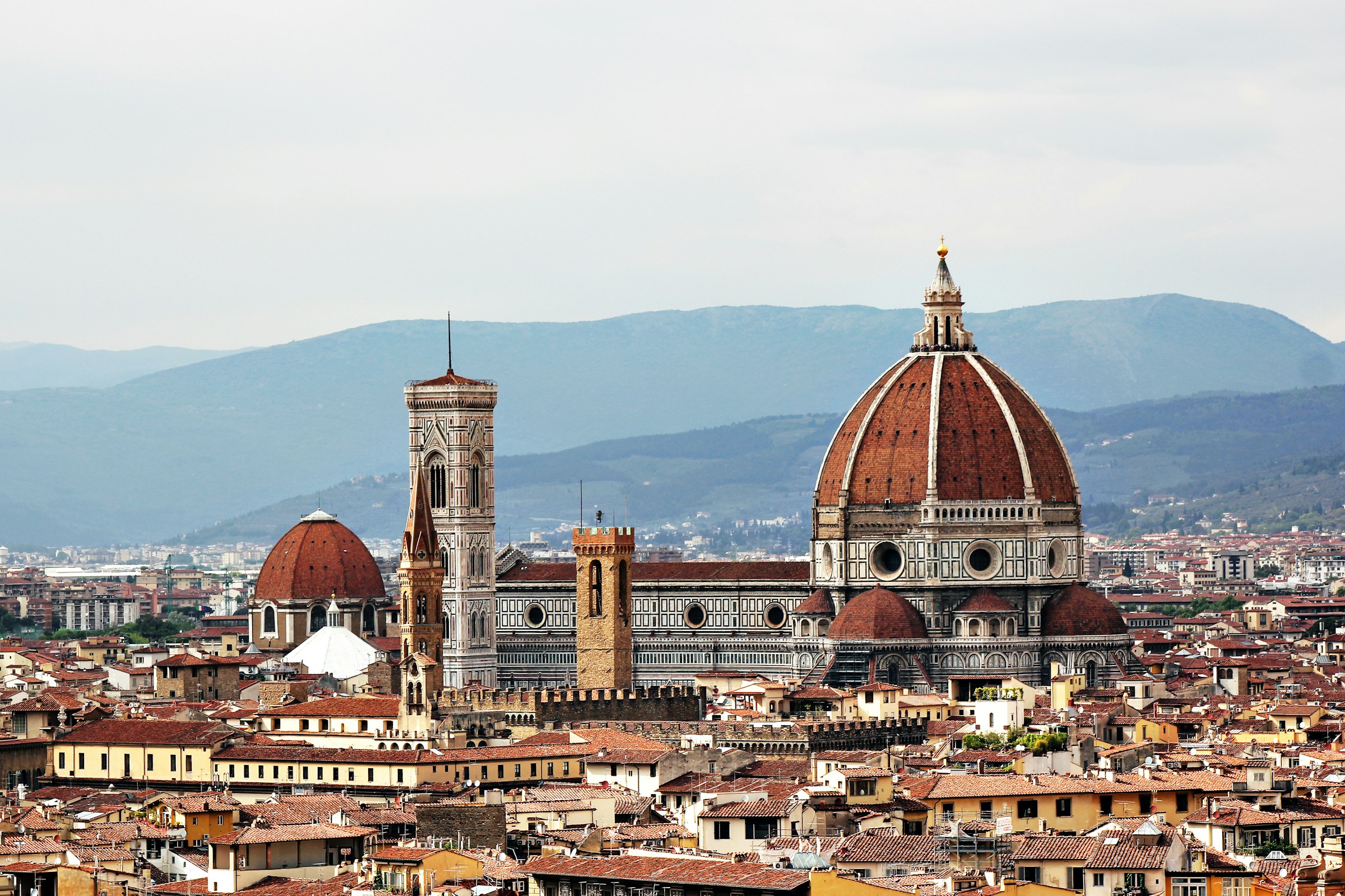 View of the Cathedral of the Duomo in Florence, with the city around it and hills in the background meeting a cloudy sky