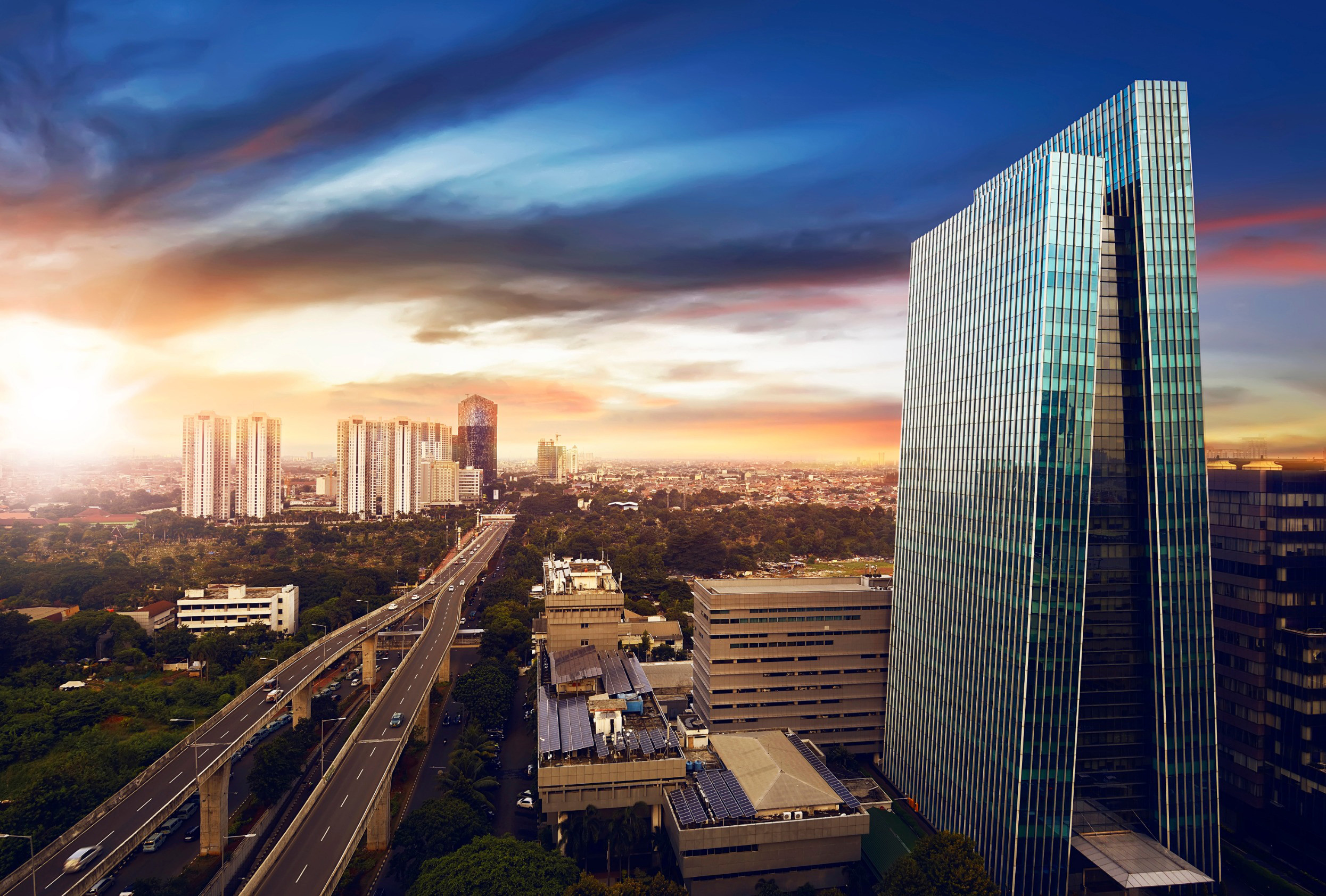 Solnedgang over Jakarta by med en motorvej og glasskyskraber med bysilhuet i baggrunden