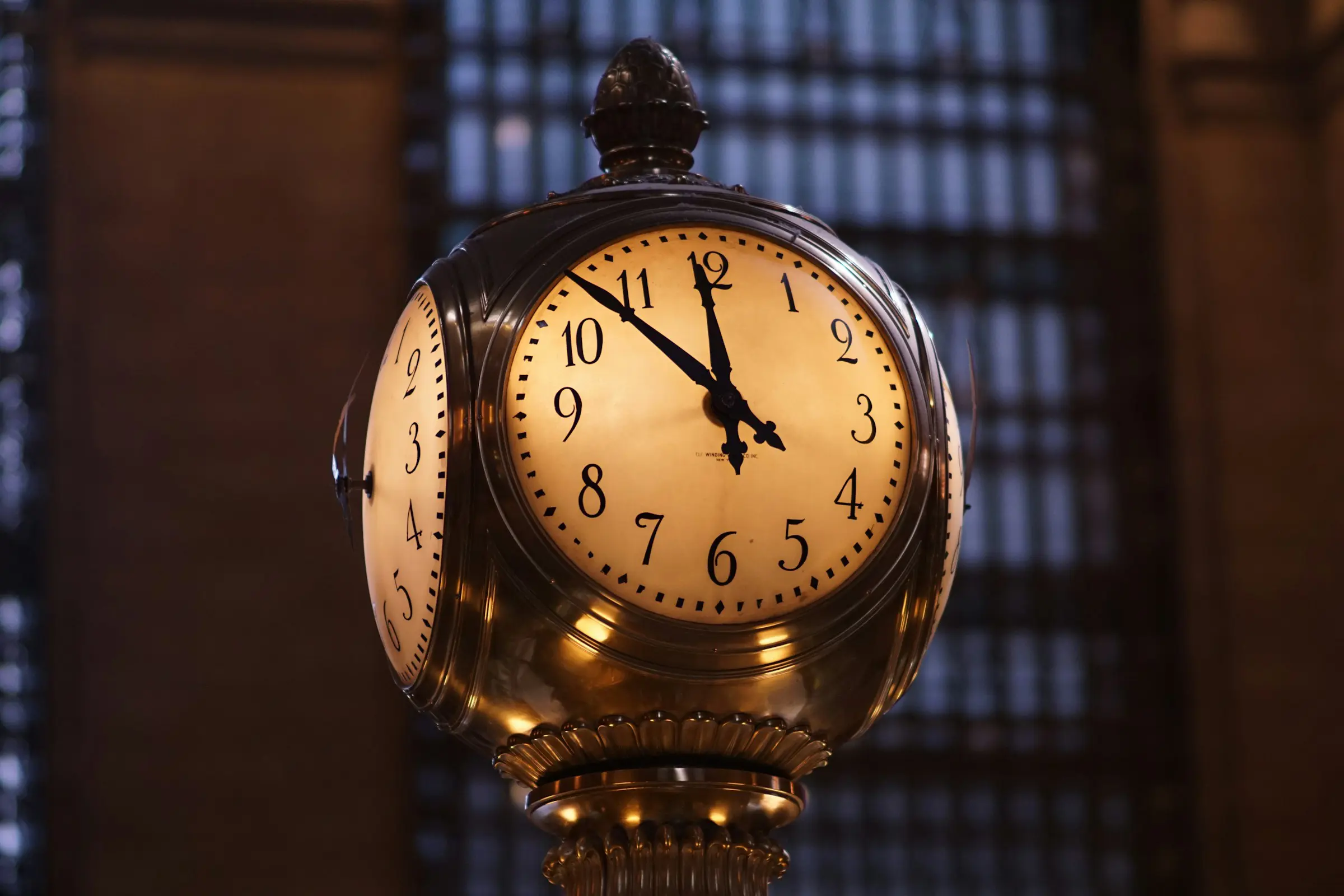 An ornate clock inside Grand Central Terminal displays the time as 10:10, against a dimly lit, architectural background