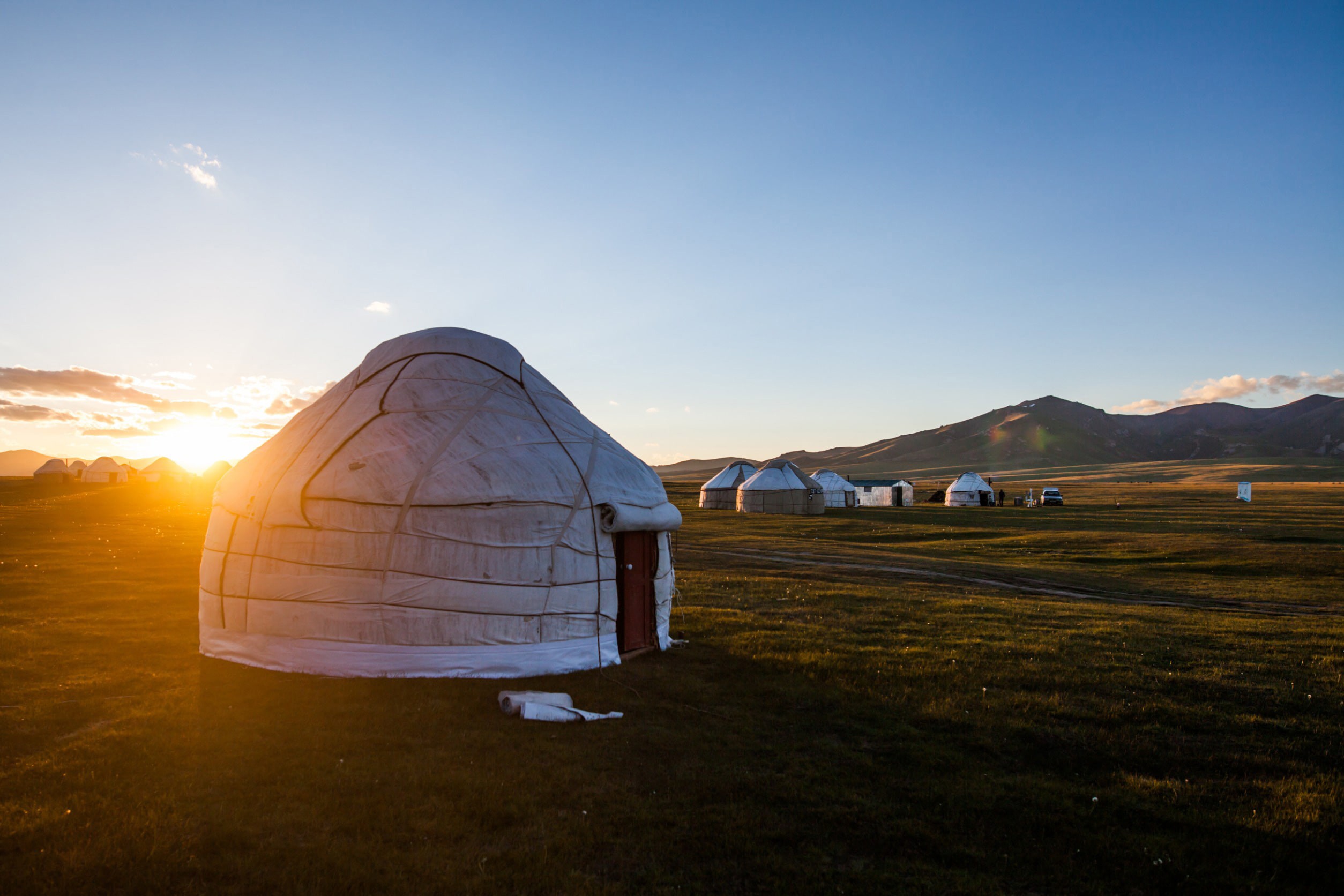 Klassisk mongolsk hytte på en slette med smuk solnedgang i baggrunden blandt bjergene