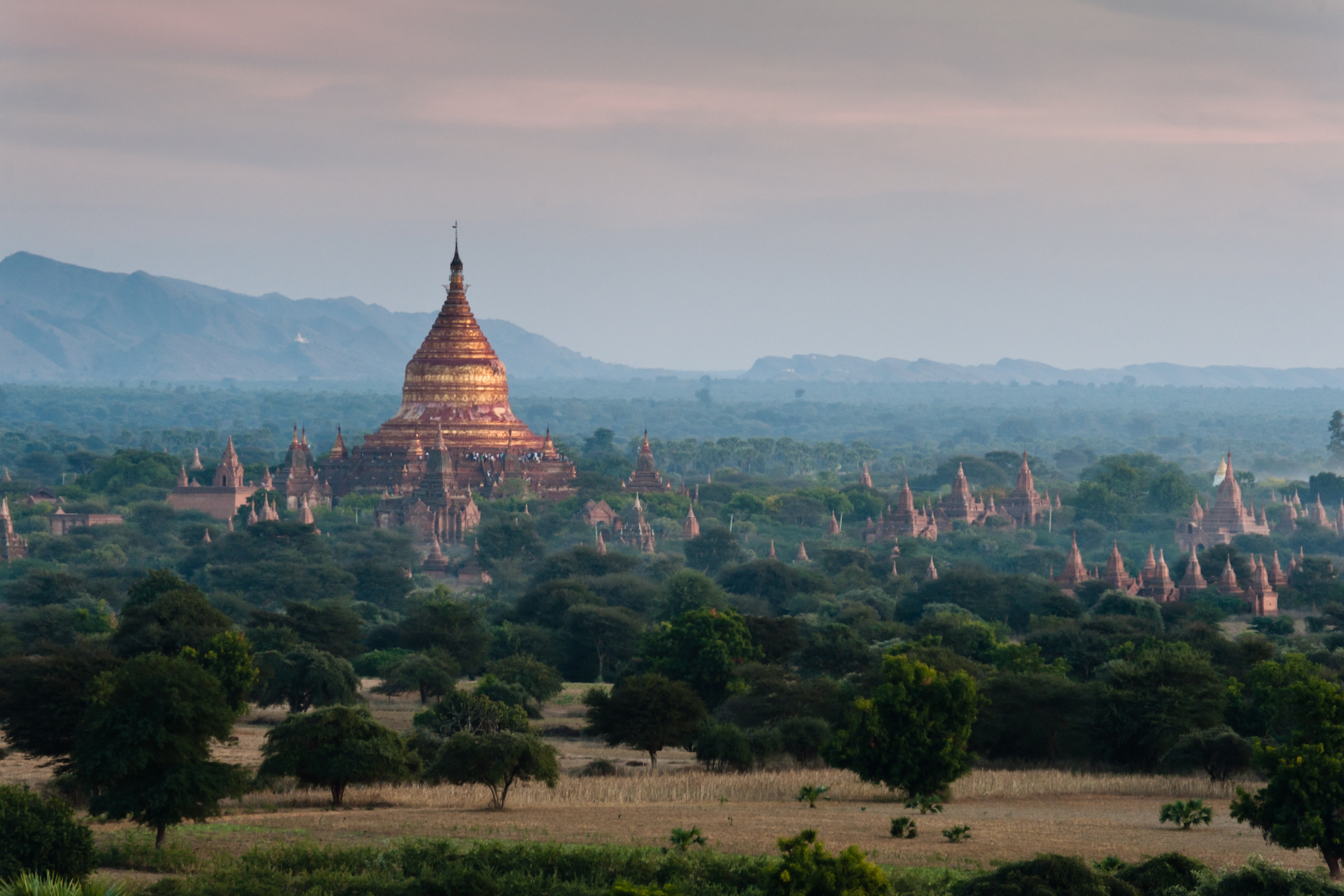 Rejser til Myanmar - Smuk jungle omkring et asiatisk tempel under en solnedgang med svag tåge og klipper i baggrunden