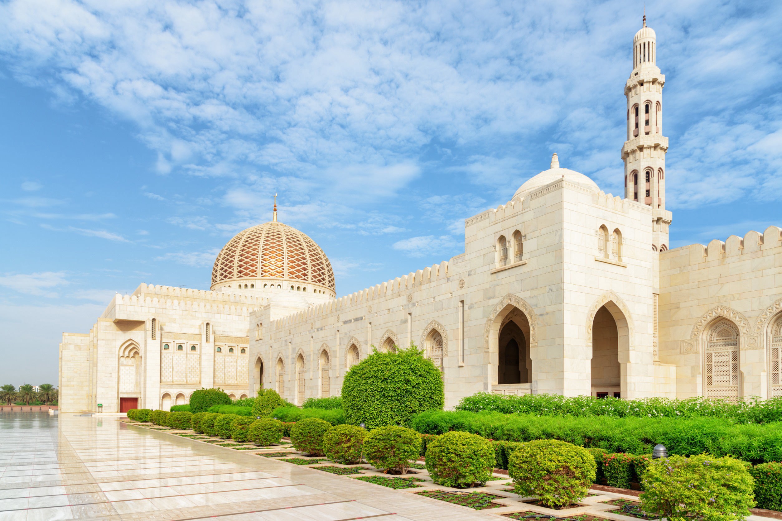 Smuk hvid moské i Muscat med grønne buske rundt og klar blå himmel i baggrunden