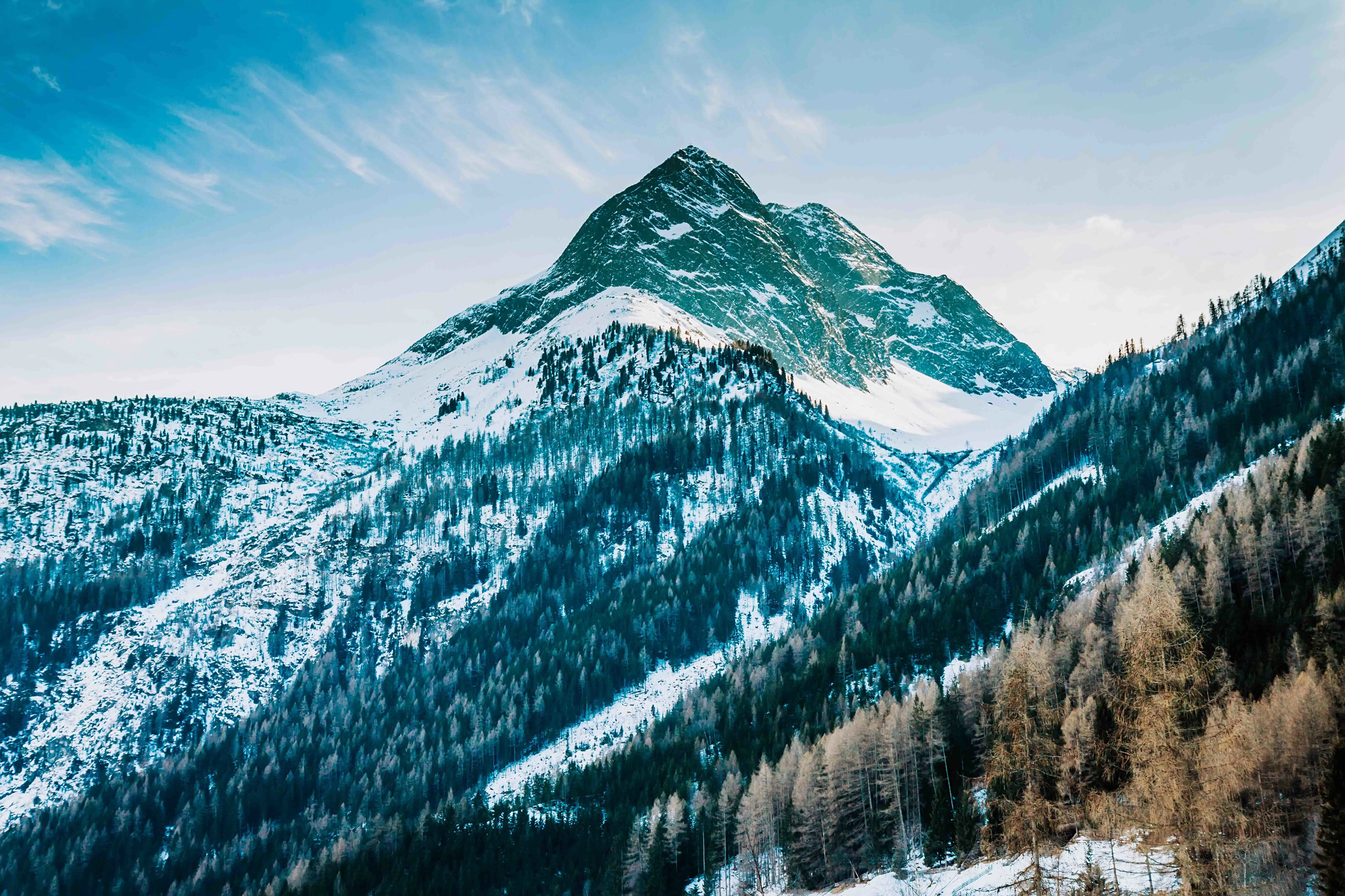 Travel to St. Anton - Snow-capped mountain peak with forested slopes against a clear blue sky.