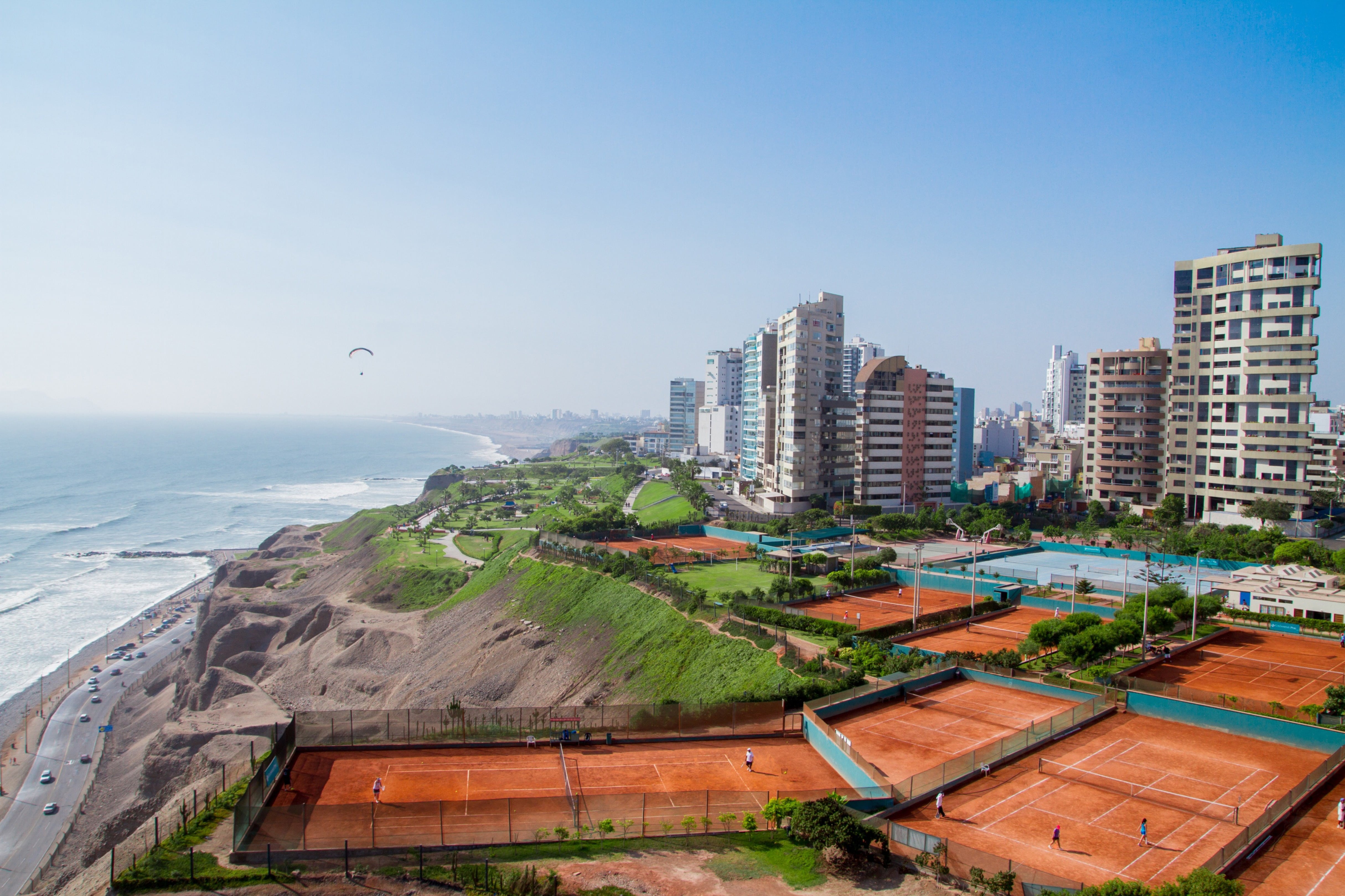 Rejs til Lima - Vu over kysten, hvor havet møder bykanten af Lima i Peru med bygninger, tennisbane og blå himmel