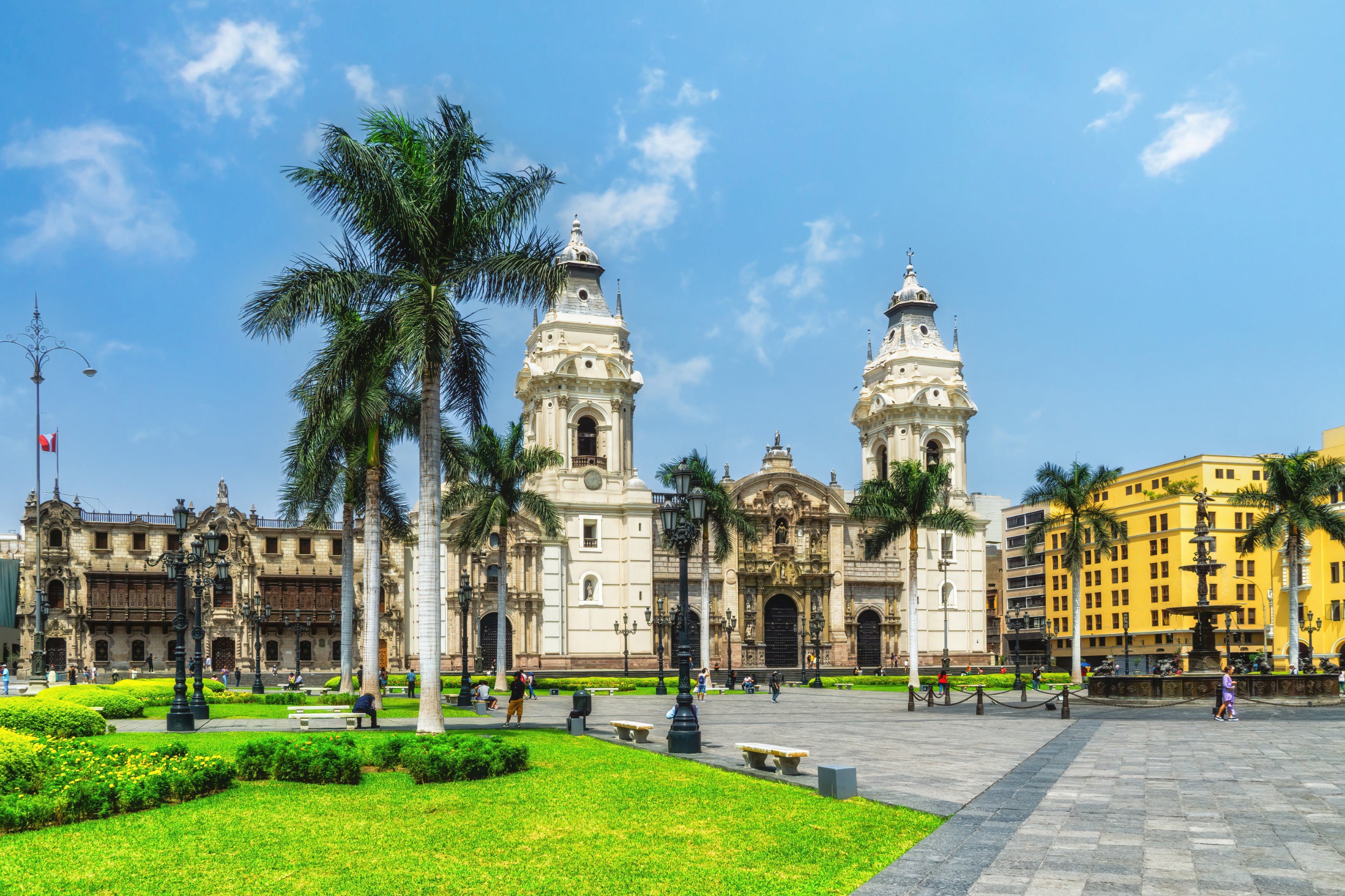 Smuk plads med grønt græs, palmer og traditionelle spanske bygninger i hvidt og gult i Lima, Peru