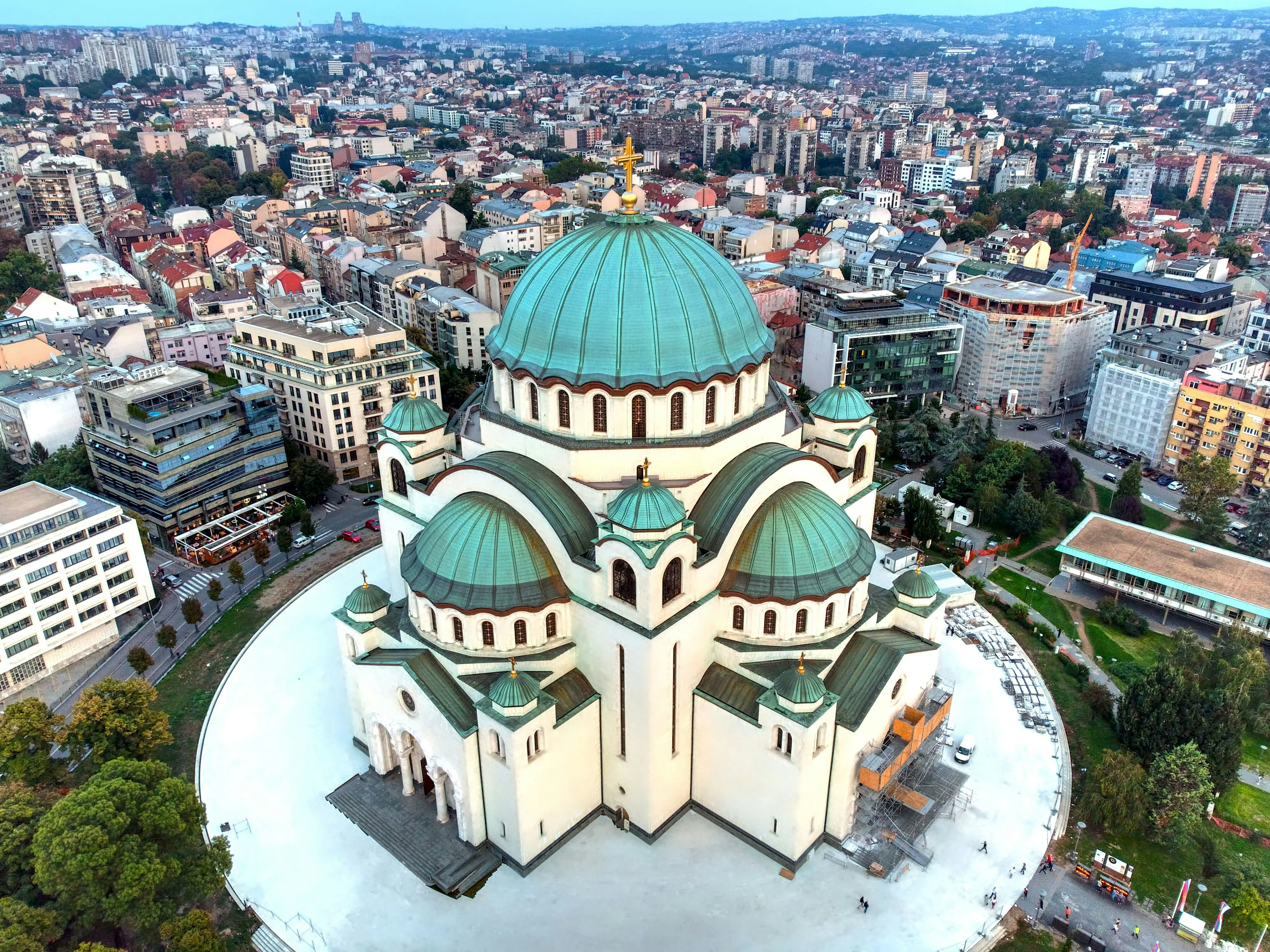 Aerial view of the Church of Saint Sava in Belgrade, Serbia, showcasing its large green domes and intricate architecture, surrounded by urban cityscape.