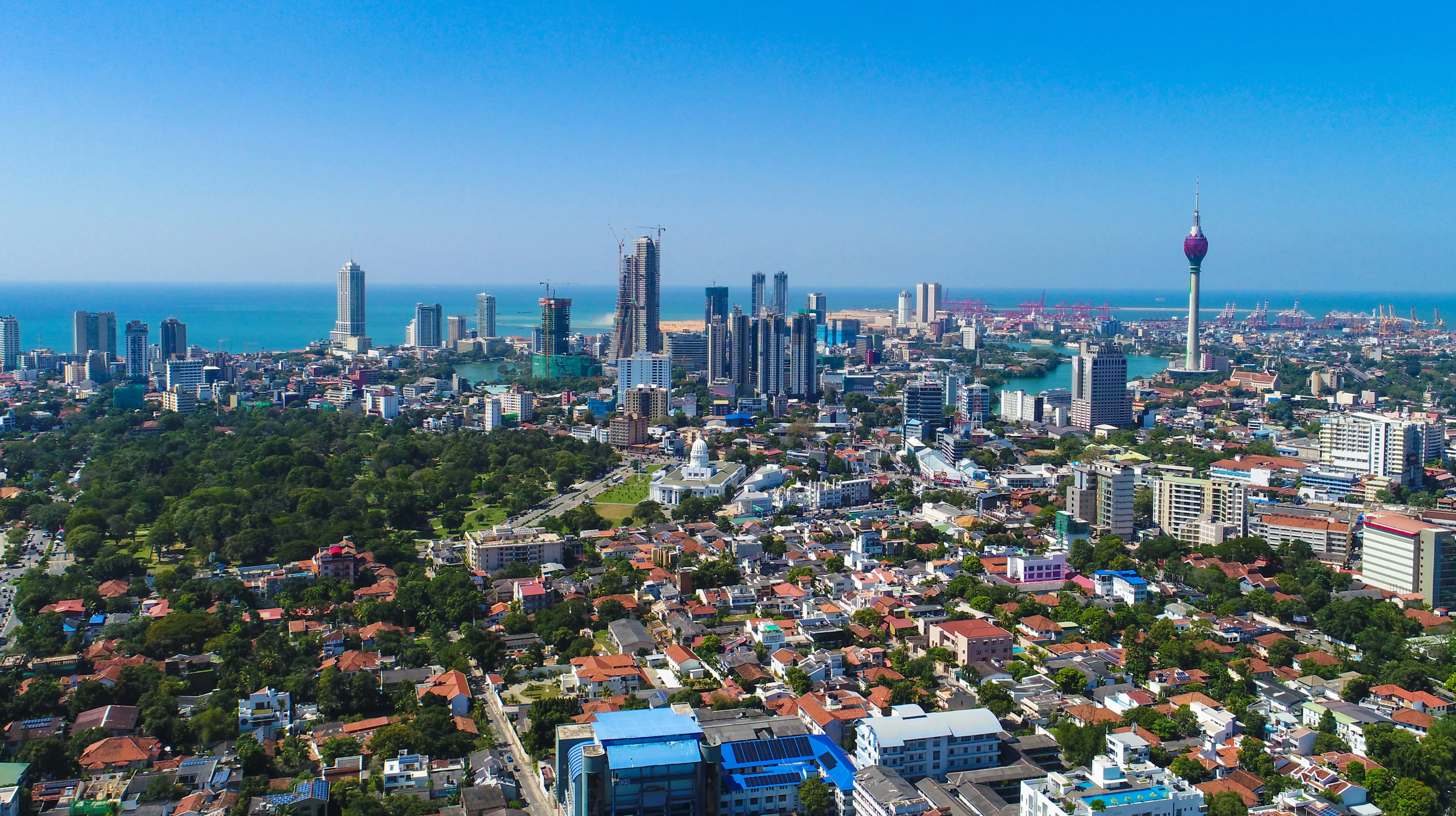 Rejs til Colombo - Panoramaudsigt over byen med grønne områder og bygninger, der møder en kyst af blåt hav og blå himmel