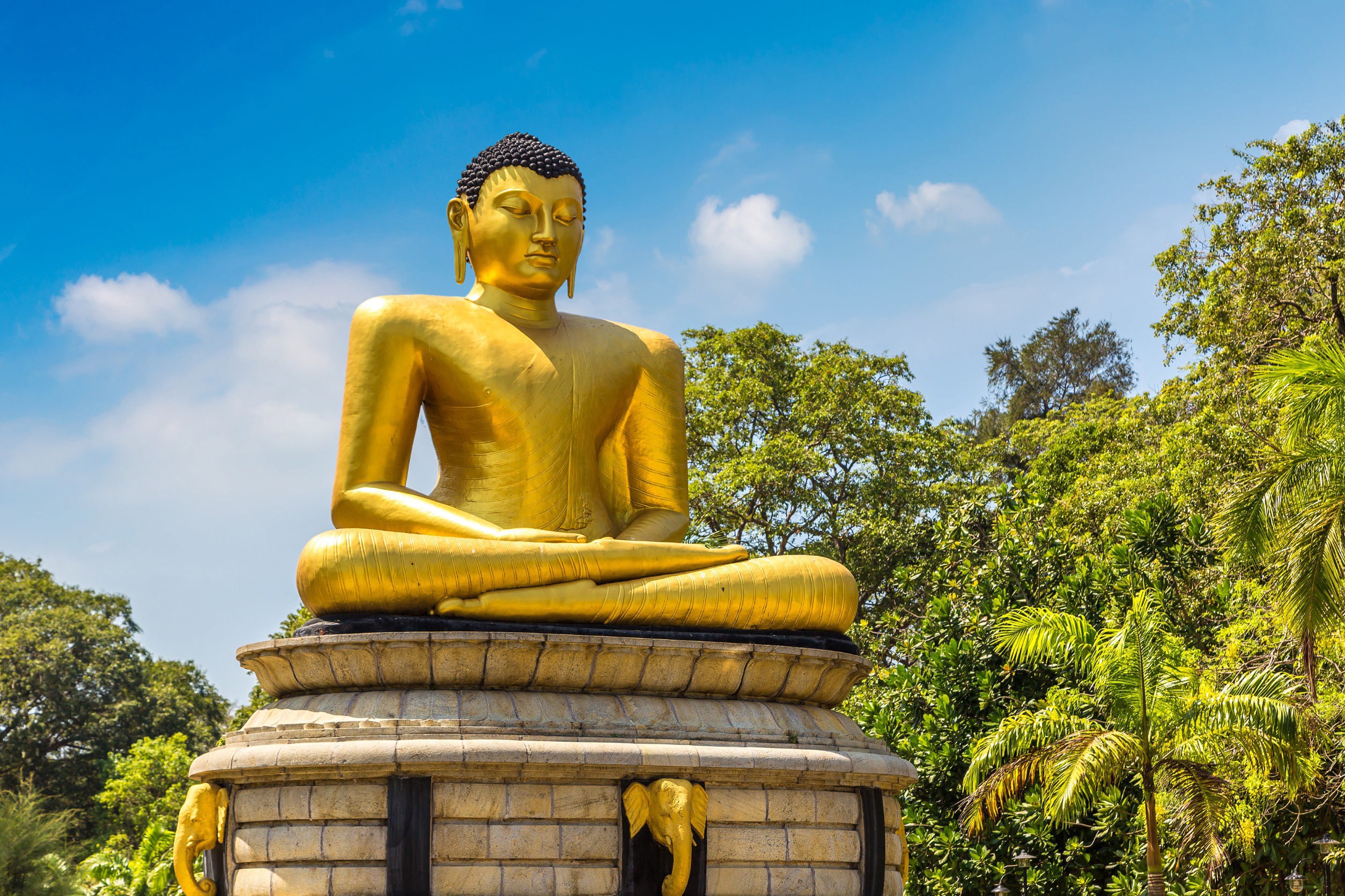 Gylden buddhistisk statue med palmer omkring den i Colombo, Sri Lanka