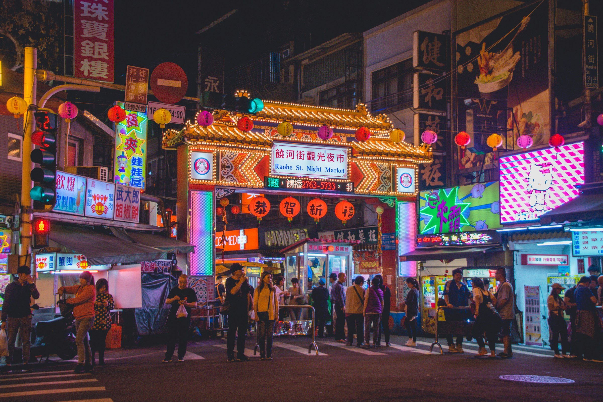 Entrance to famous night market in Taipei city with neon lights, signs, and people around