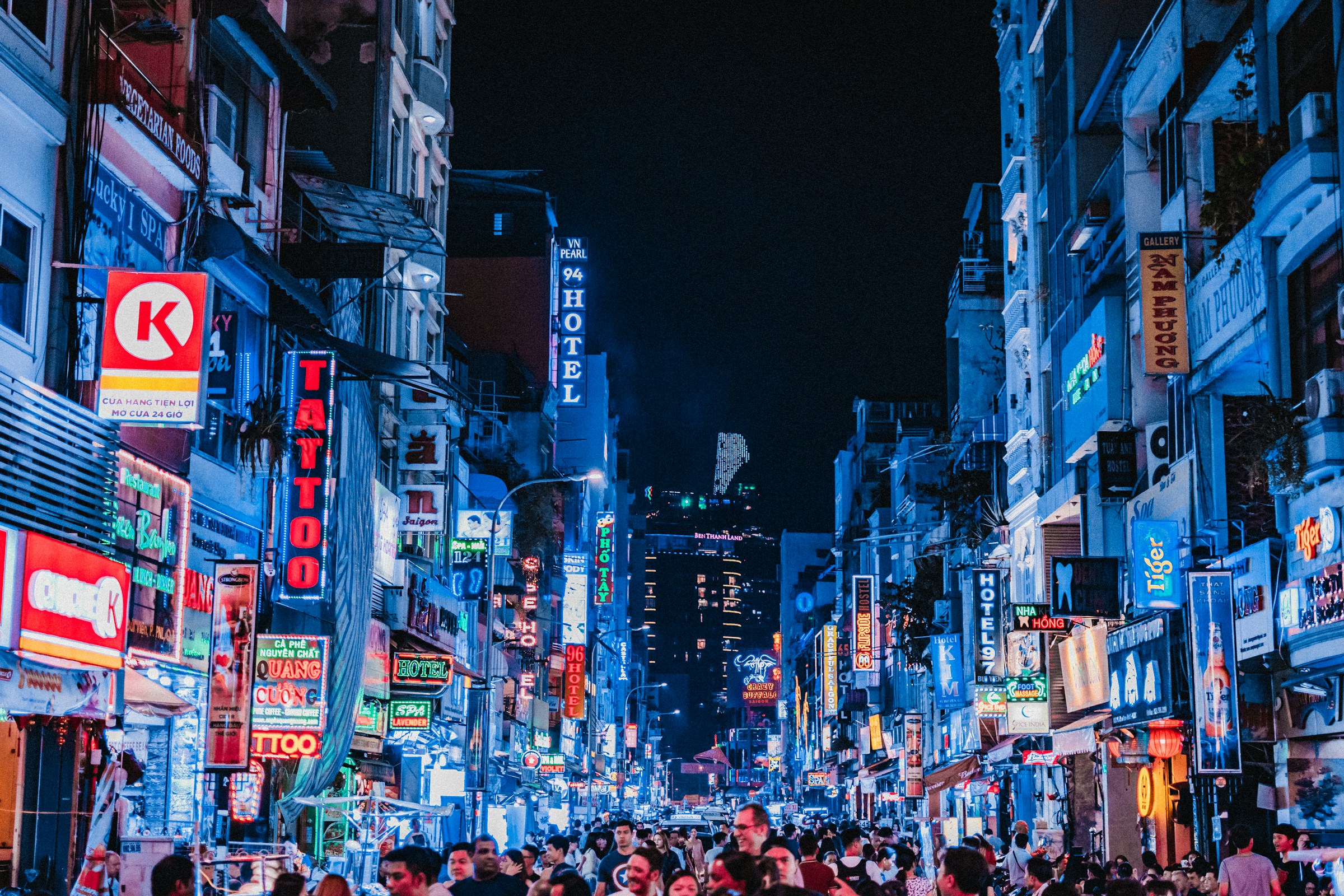 Lively city street in the evening in Ho Chi Minh City with neon lights and signs, crowd strolling in big city atmosphere.